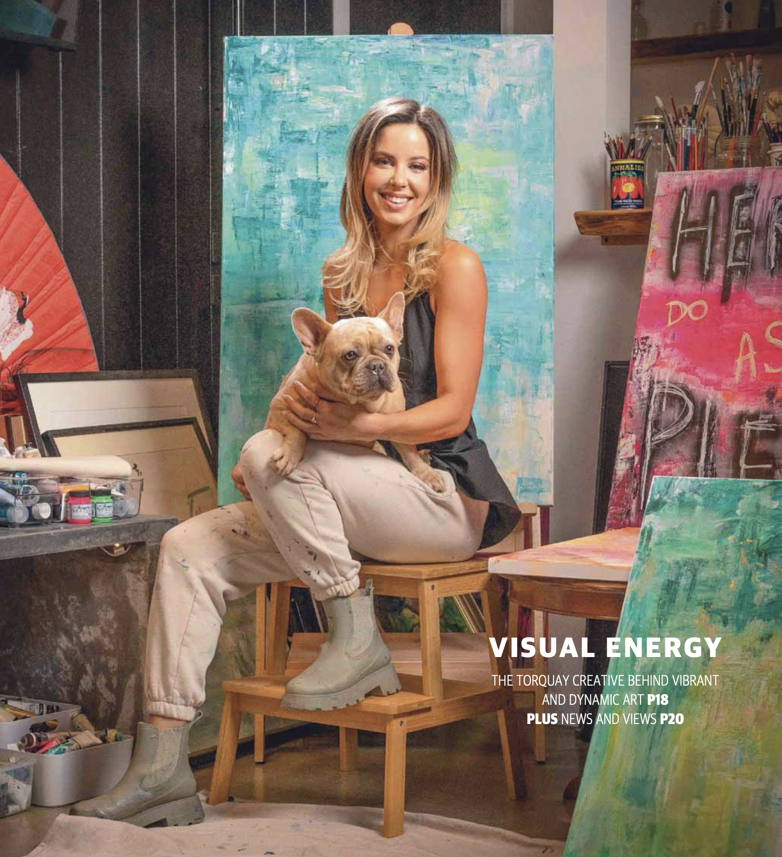 Gabrielle May seated in her studio holding a French bulldog beside vibrant paintings