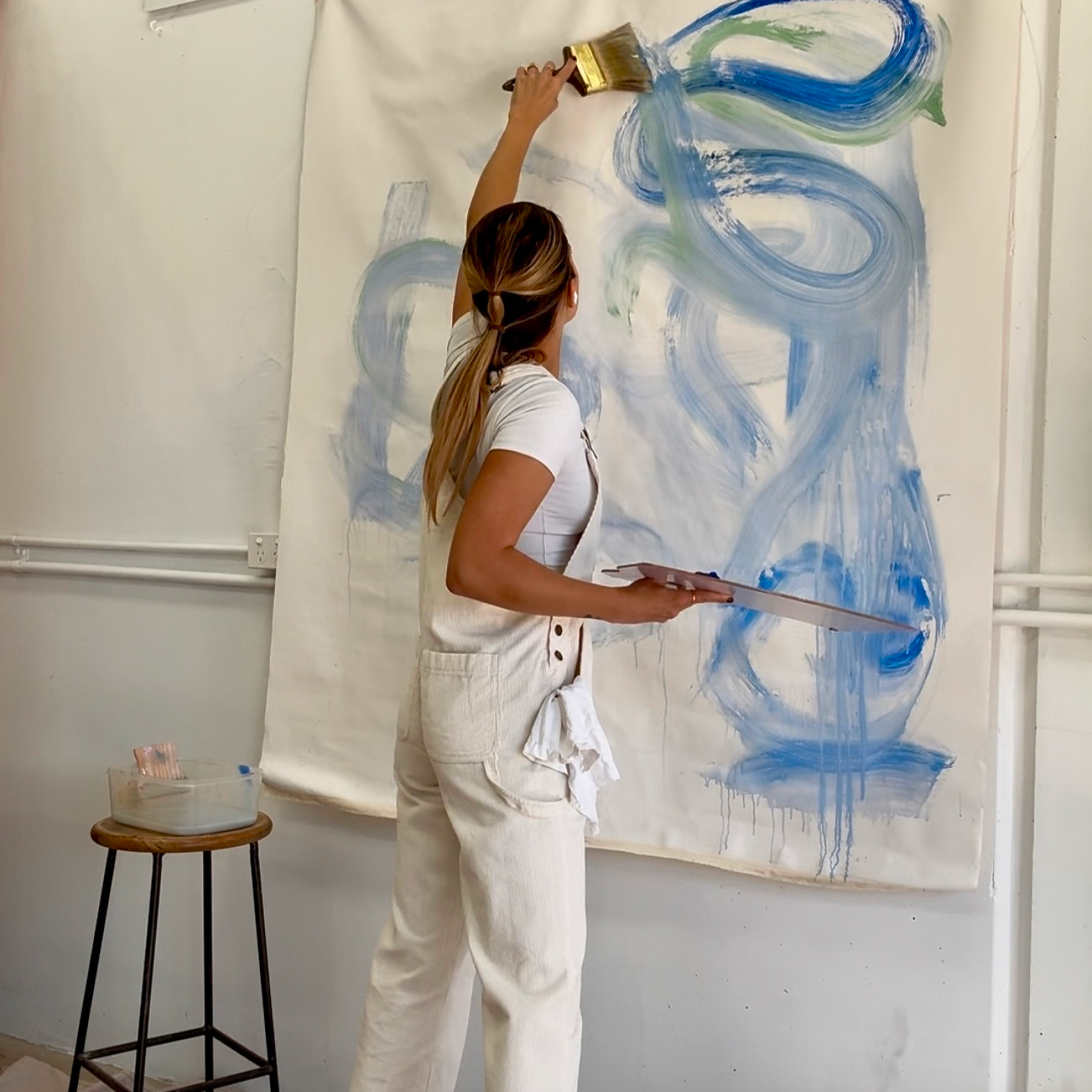 Gabrielle May painting a large blue abstract mural on a wall