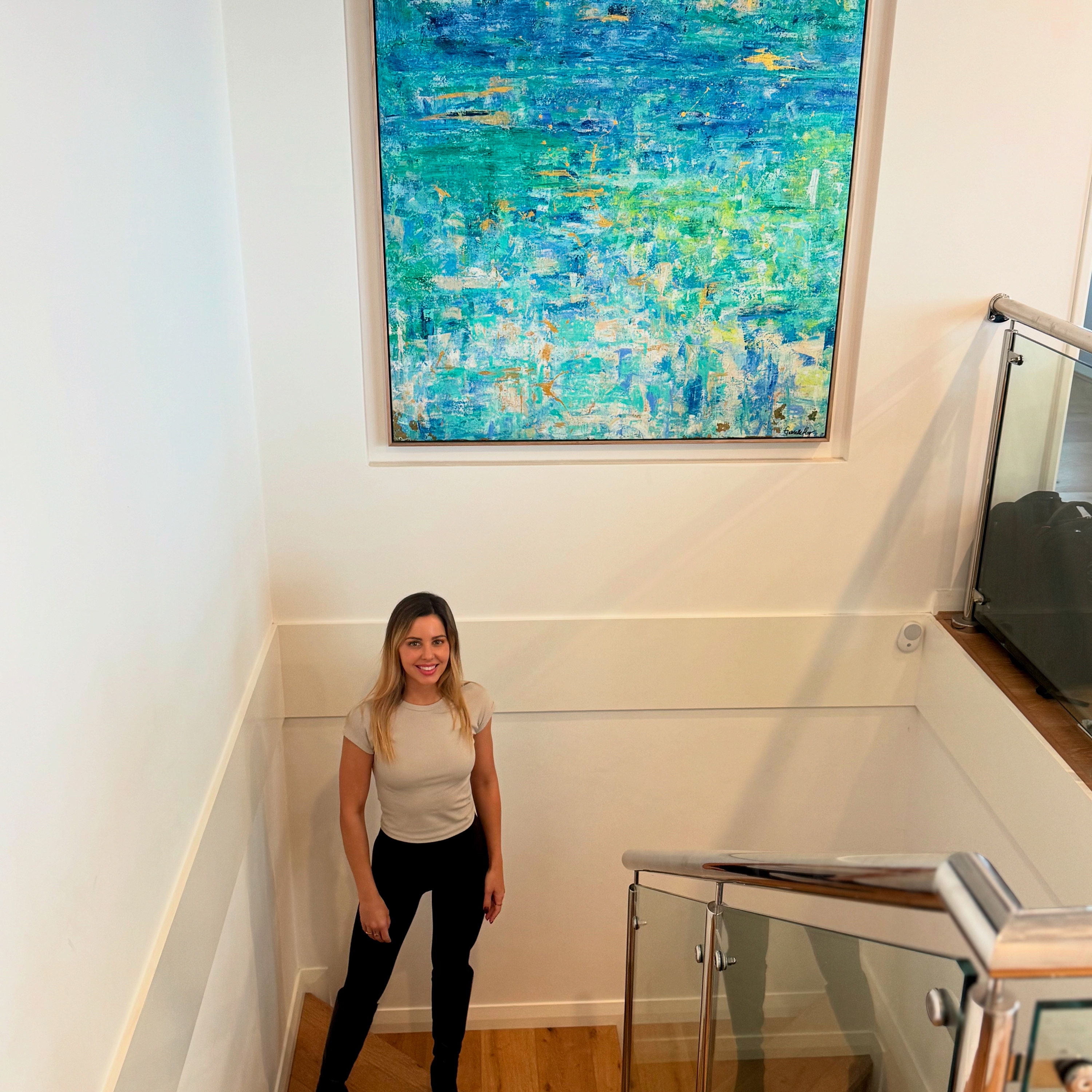 Large blue abstract painting installed above a staircase in a home interior