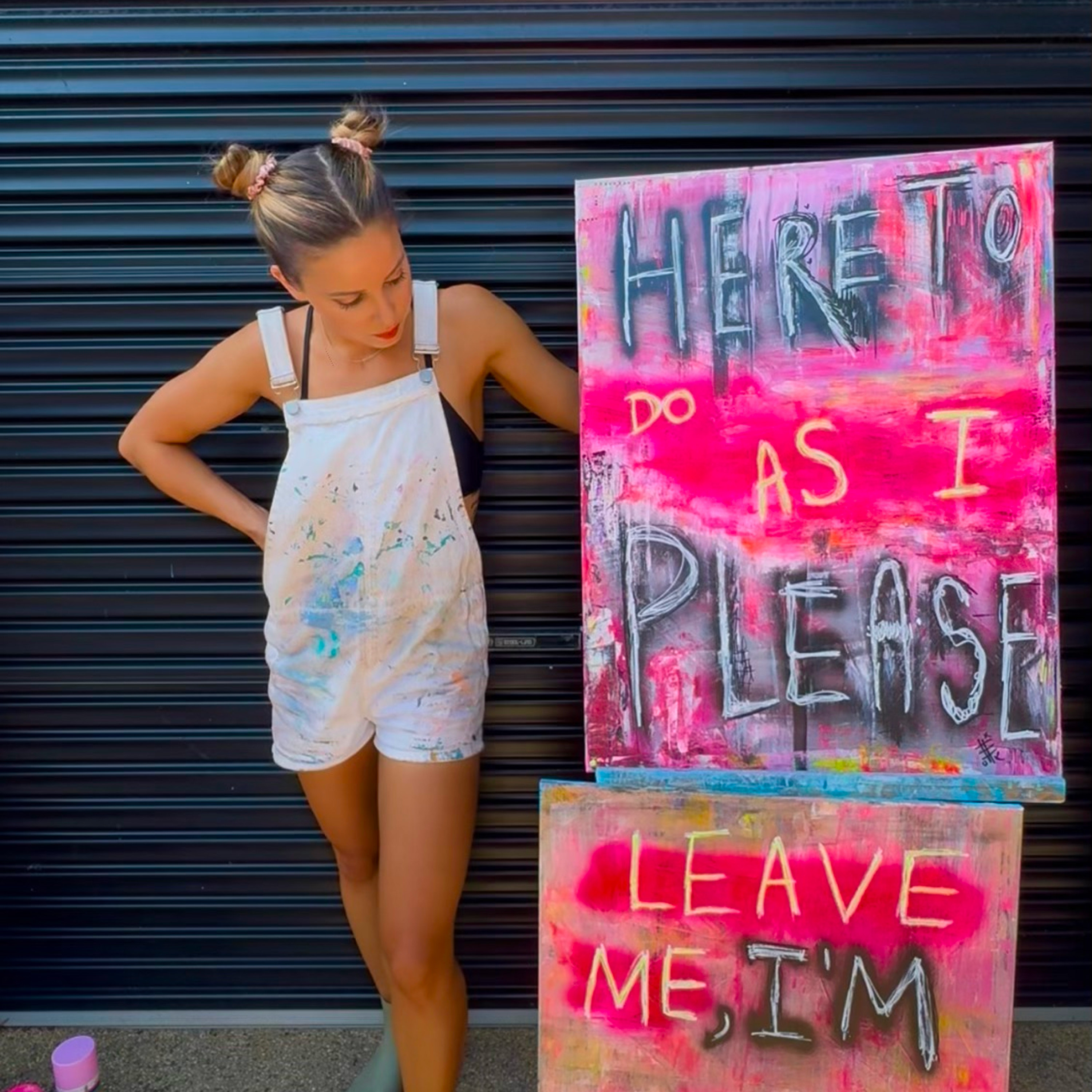 Gabrielle May standing beside vibrant graffiti-style paintings in the studio
